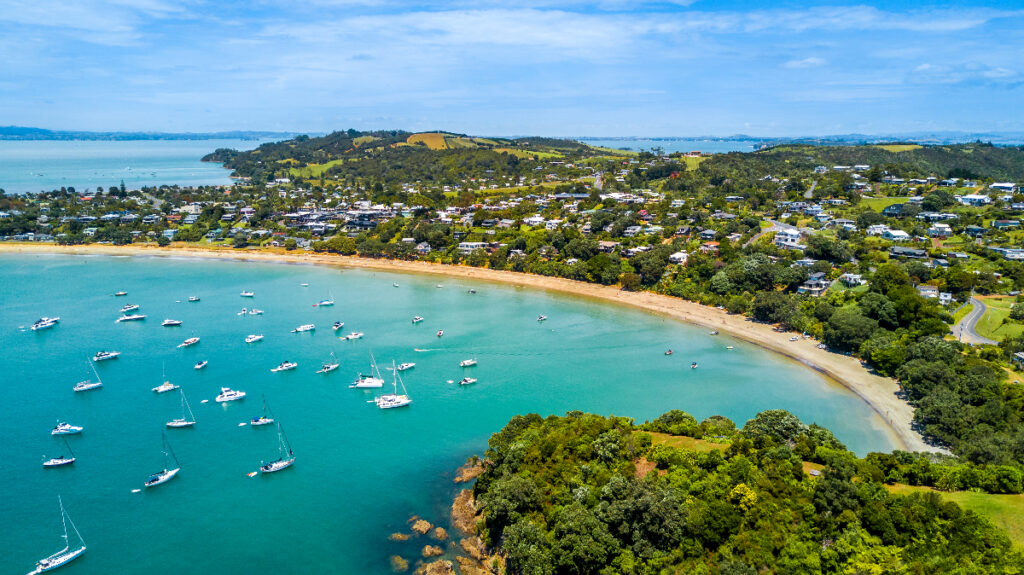 Aerial view on beautiful bay at sunny day with sandy beach and residential suburbs on the background. Waiheke Island, Auckland, New Zealand.